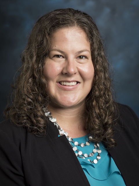 Woman with brown wavy hair and teal shirt and black blazer
